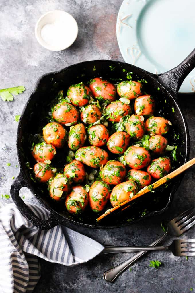 Parsley Potatoes are very easy to make. They very fragrant and filling, yet you only need 4 ingredients to make them! It's a perfect side dish for any meat or fish. Parsley potatoes in a skillet with wooden spoon and plate on a side