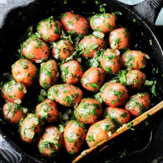 Overhead shot of parsley potatoes in a skillet with wooden spoon