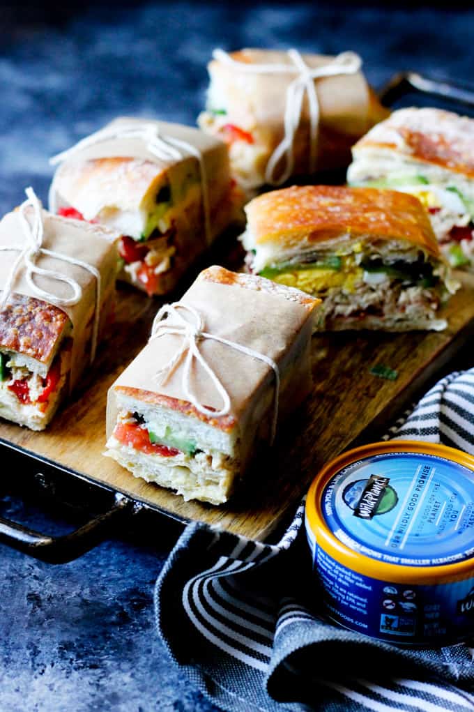 Pan bagnat sandwiches on a serving board with canned tuna next to it