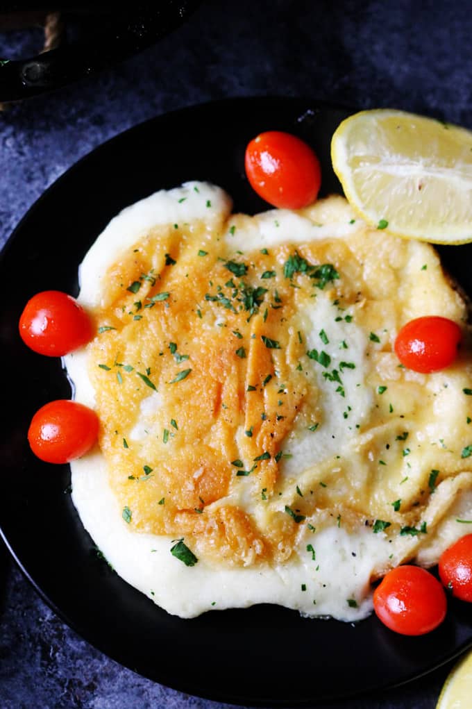 Greek Pan Fried Cheese Saganaki on a black plate with tomatoes and lemon wedges