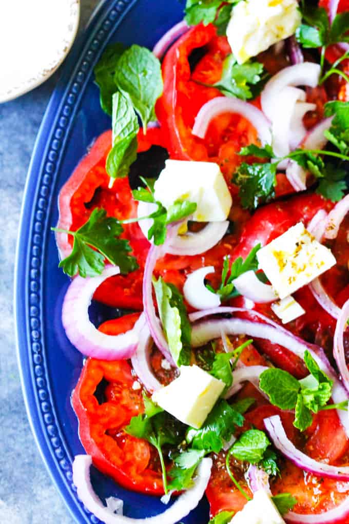 This Tomato Feta Salad is as simple as it gets, and it is super delicious! When ripe, juicy tomatoes are in season you'll want to eat it every day. It contains a few simple ingredients and it comes together in no time at all. Close up shot of Tomato Feta Salad with fresh herbs on blue plate