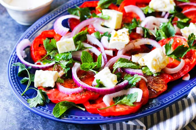 This Tomato Feta Salad is as simple as it gets, and it is super delicious! When ripe, juicy tomatoes are in season you'll want to eat it every day. It contains a few simple ingredients and it comes together in no time at all. Vertical shot of tomato feta salad with fresh herbs on blue plate