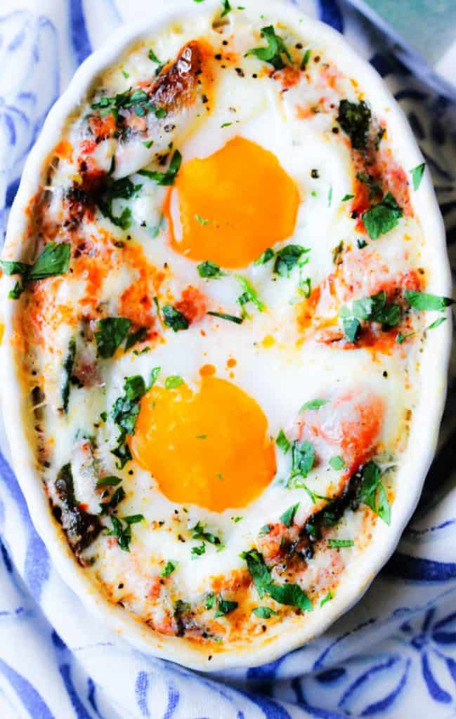 Baked eggs in cream tomato spinach sauce in white ramekin