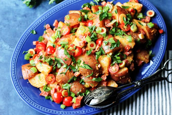 Horizontal photo of Spanish Potato Salad with Smoked Paprika Dressing on a blue serving plate with spoon