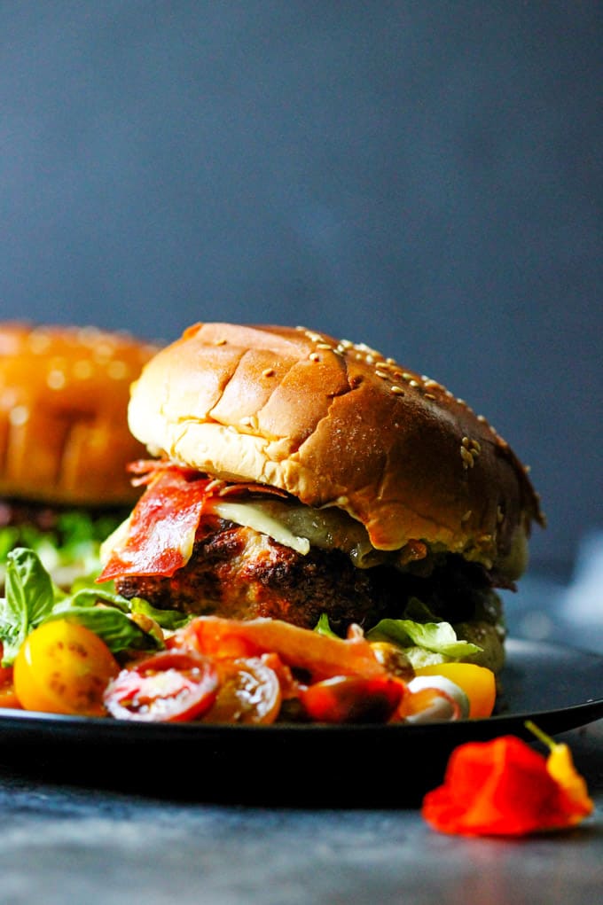 Turkey burger with caramelized onions, cured ham and brie cheese on black plate with side caprese salad