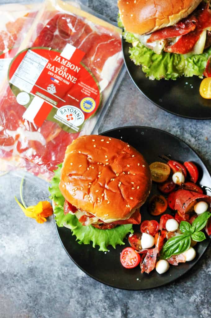 Turkey burgers on black plates with side caprese salad and Bayonne ham on a side