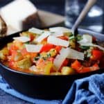 Spanish Pisto Manchego in a bowl with spoon and cheese on top