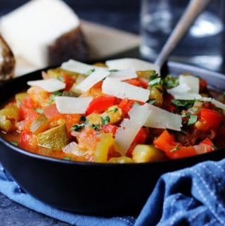 Spanish Pisto Manchego in a bowl with spoon and cheese on top