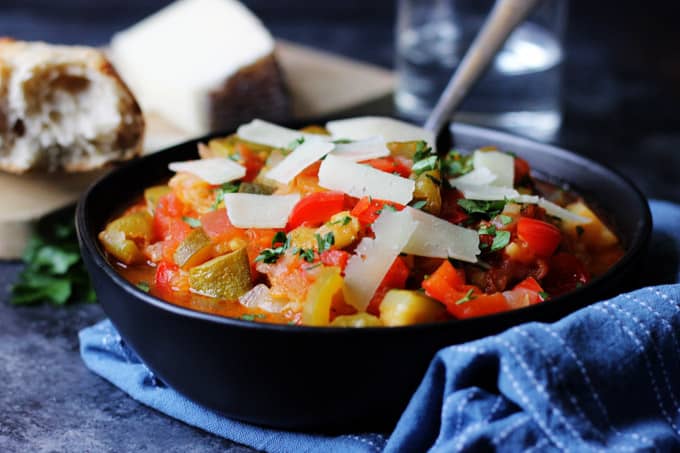 Spanish Pisto Manchego in a bowl with spoon and cheese on top