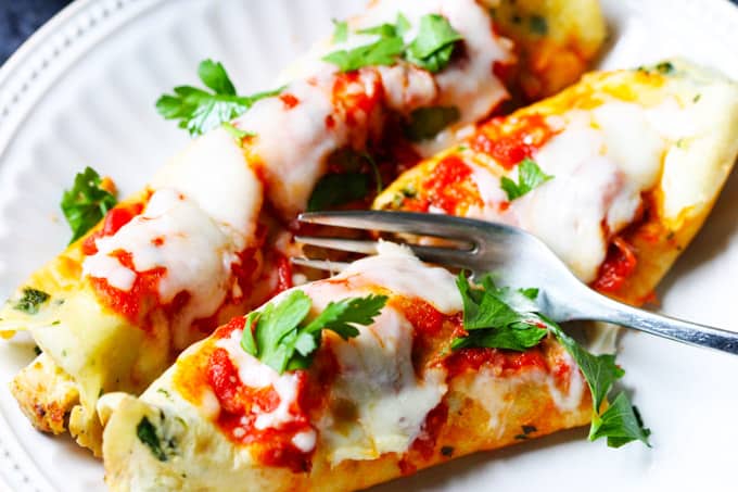 Savory crepes on a plate with fork cutting it in a half