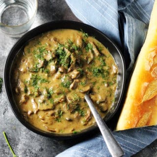 Beef Stroganoff in a black bowl with spoon and bread on a side
