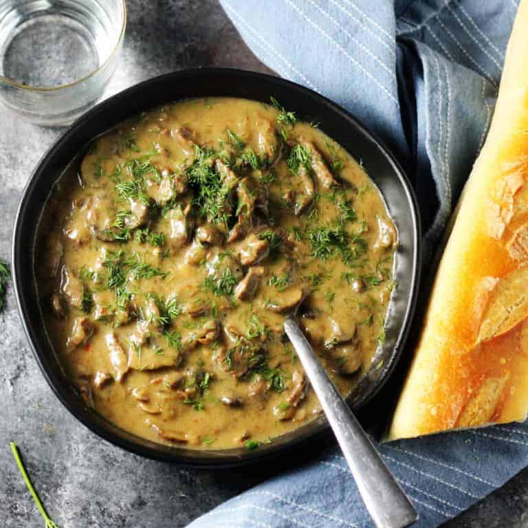 Beef Stroganoff in a black bowl with spoon and bread on a side
