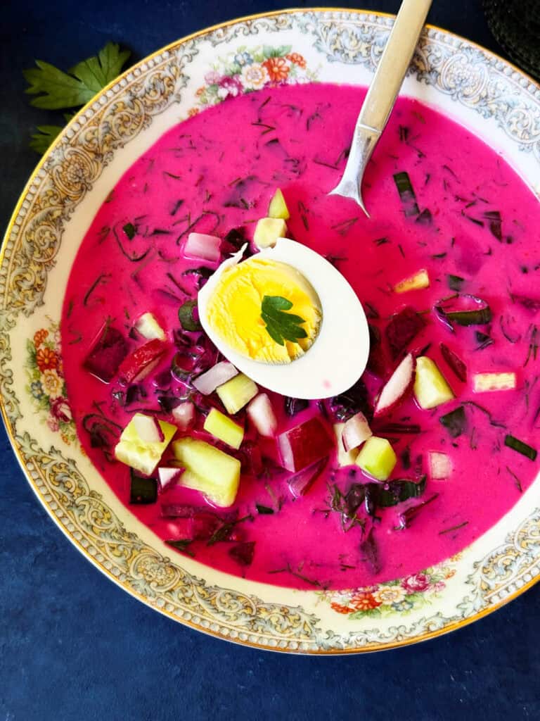 Closeup view of cold borscht soup topped with a boiled egg and cucumber