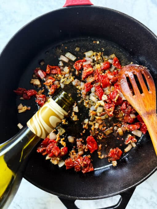 Pouring white wine into the pan with diced shallots, garlic and tomatoes