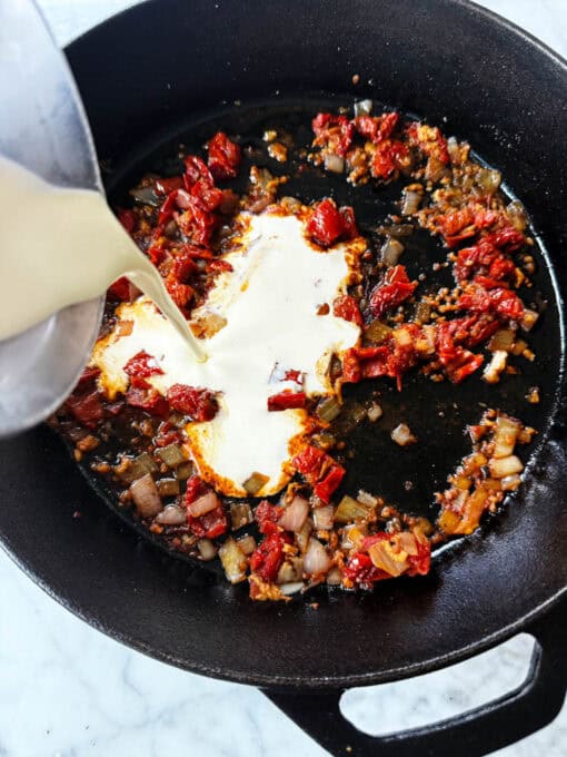 Pouring heavy cream into the pan with the sauteed vegetables