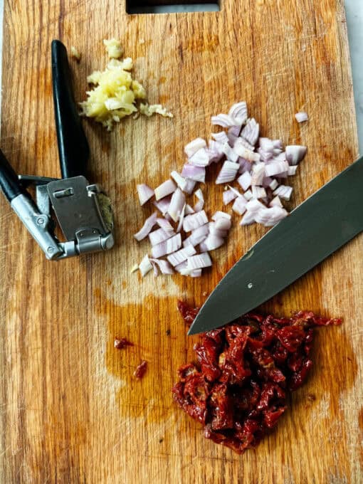 Diced shallot, garlic and sun-dried tomatoes on a chopping board