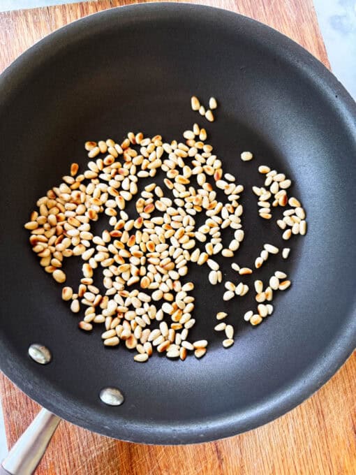 Pine nuts being toasted in a skillet for cucumber feta cheese sala