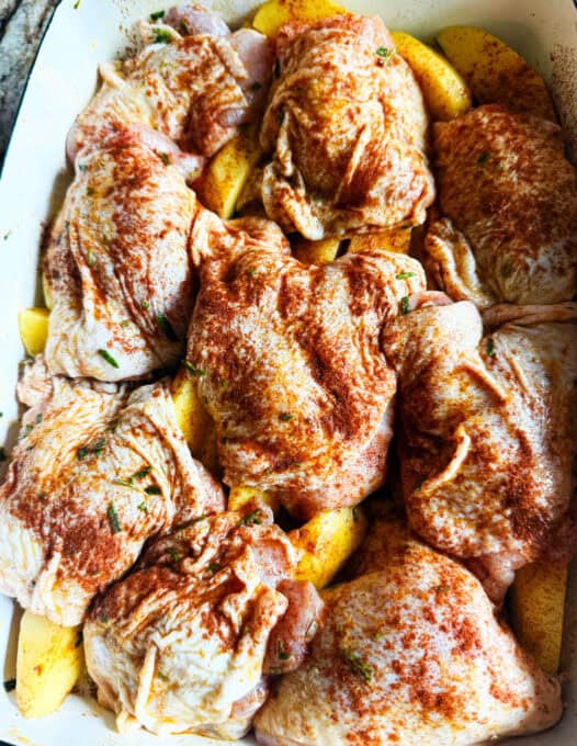 Chicken in the oven dish on top of the potatoes, sprinkled with paprika