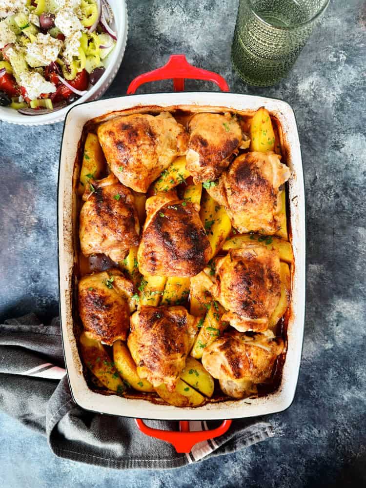 Overhead of chicken thighs and roasted potatoes in a white roasting dish