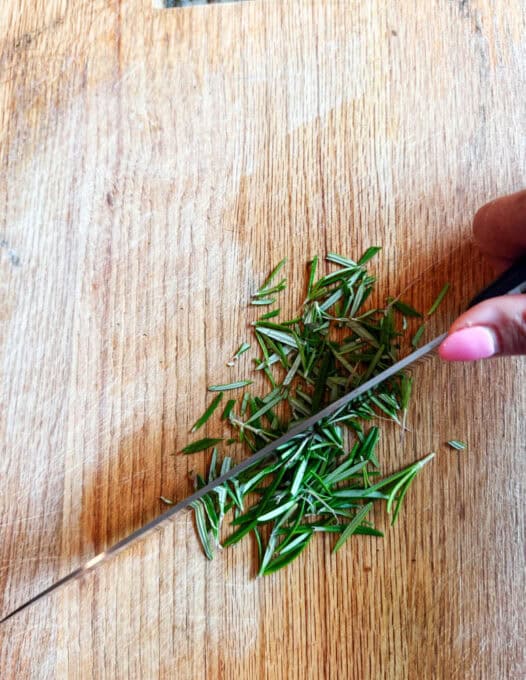 Fresh rosemary being chopped up with a knife