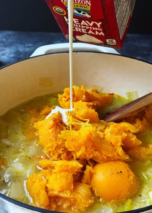 Cream is being poured over the butternut squash in the pot