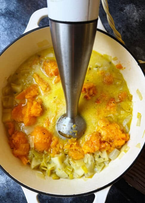 Soup is being pureed with an immersion blender